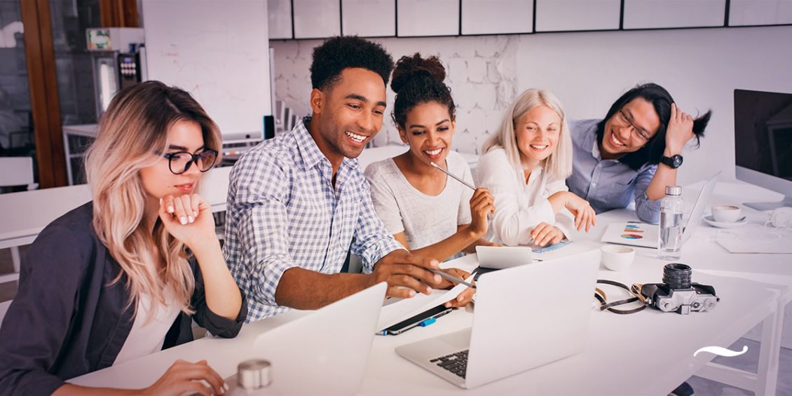 equipe-em-uma-mesa-sorrindo-e-trabalhando-em-agencia-de-publicidade-1130x565.jpg