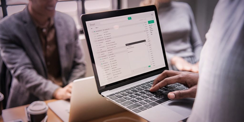 homem com notebook atendendo dois clientes em agência de publicidade