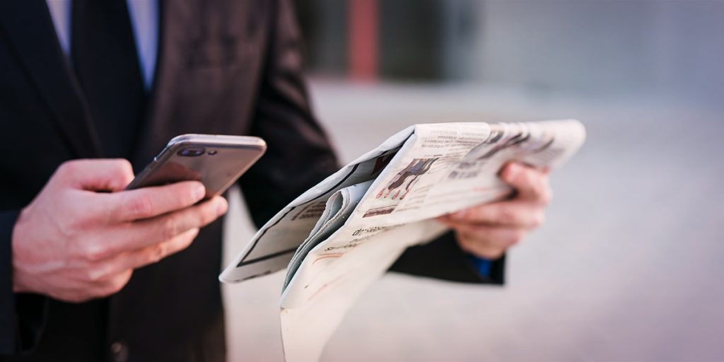 homem de paletó vendo anúncio de marketing offline no jornal e de marketing digital no celular