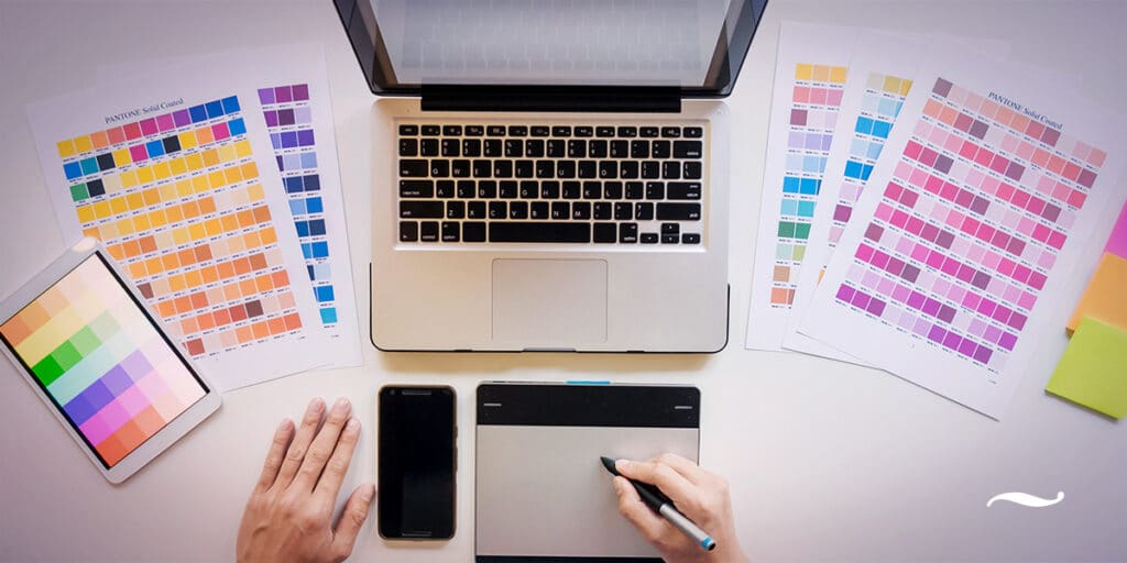 Homem fazendo direção de arte em frente ao computador escolhendo cor para um folder numa paleta de cores pantone