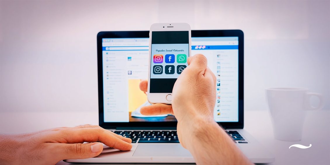 homem no notebook segurando celular fazendo gestão de redes sociais